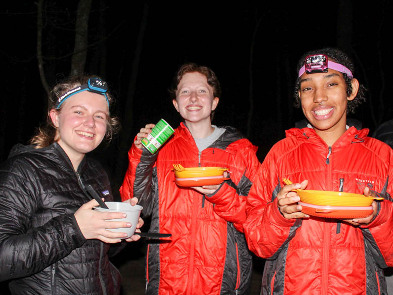 Three campers having a dinner by headlights.