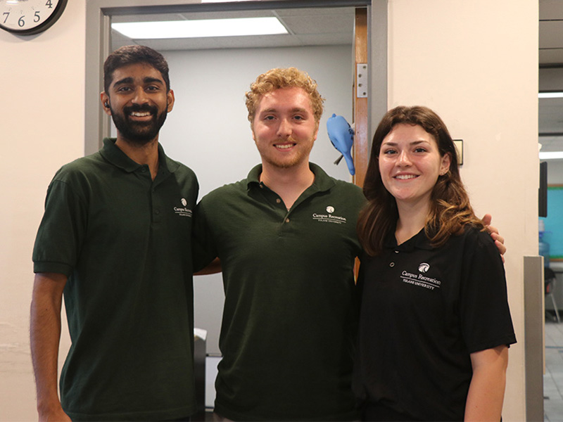 Three member services attendants pose for a group photo behind the front desk.