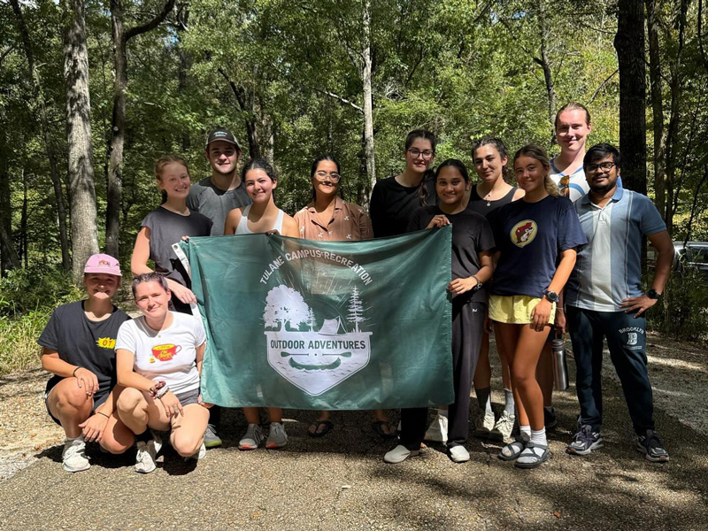 A group of students and trip leaders holding a Tulane Outdoor Adventures flag at a national park.