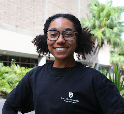 Smiling woman with curly hair and glasses wears a black Tulane University t-shirt outdoors.